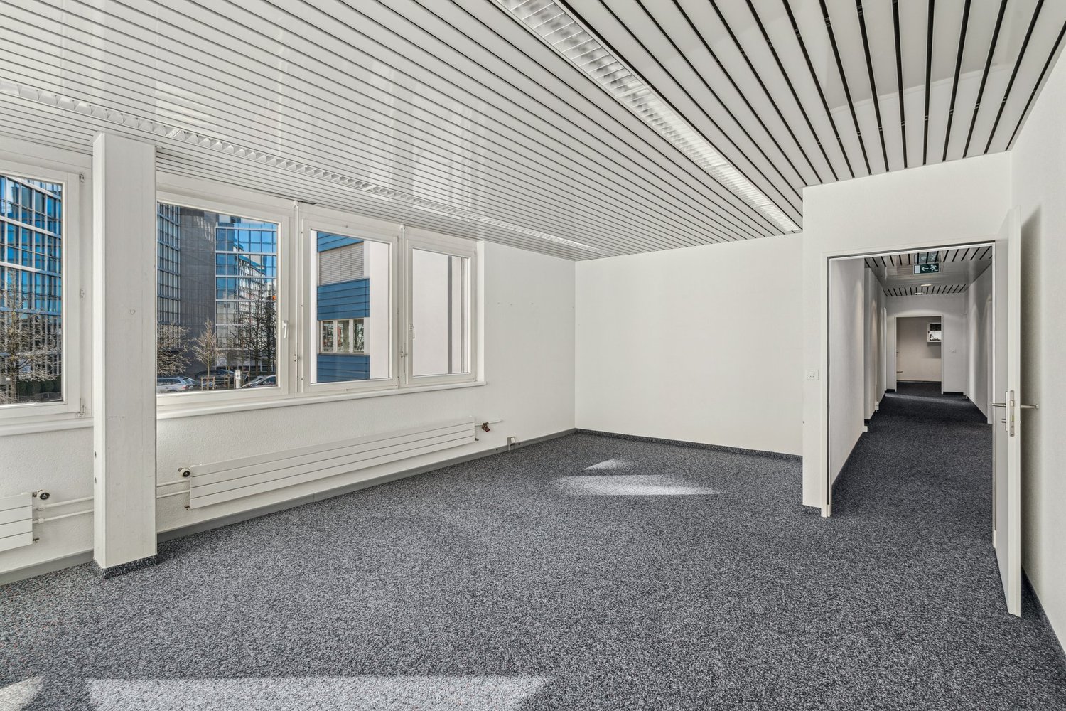 empty office room, white walls, ceiling with lines, radiators, windows, carpet
