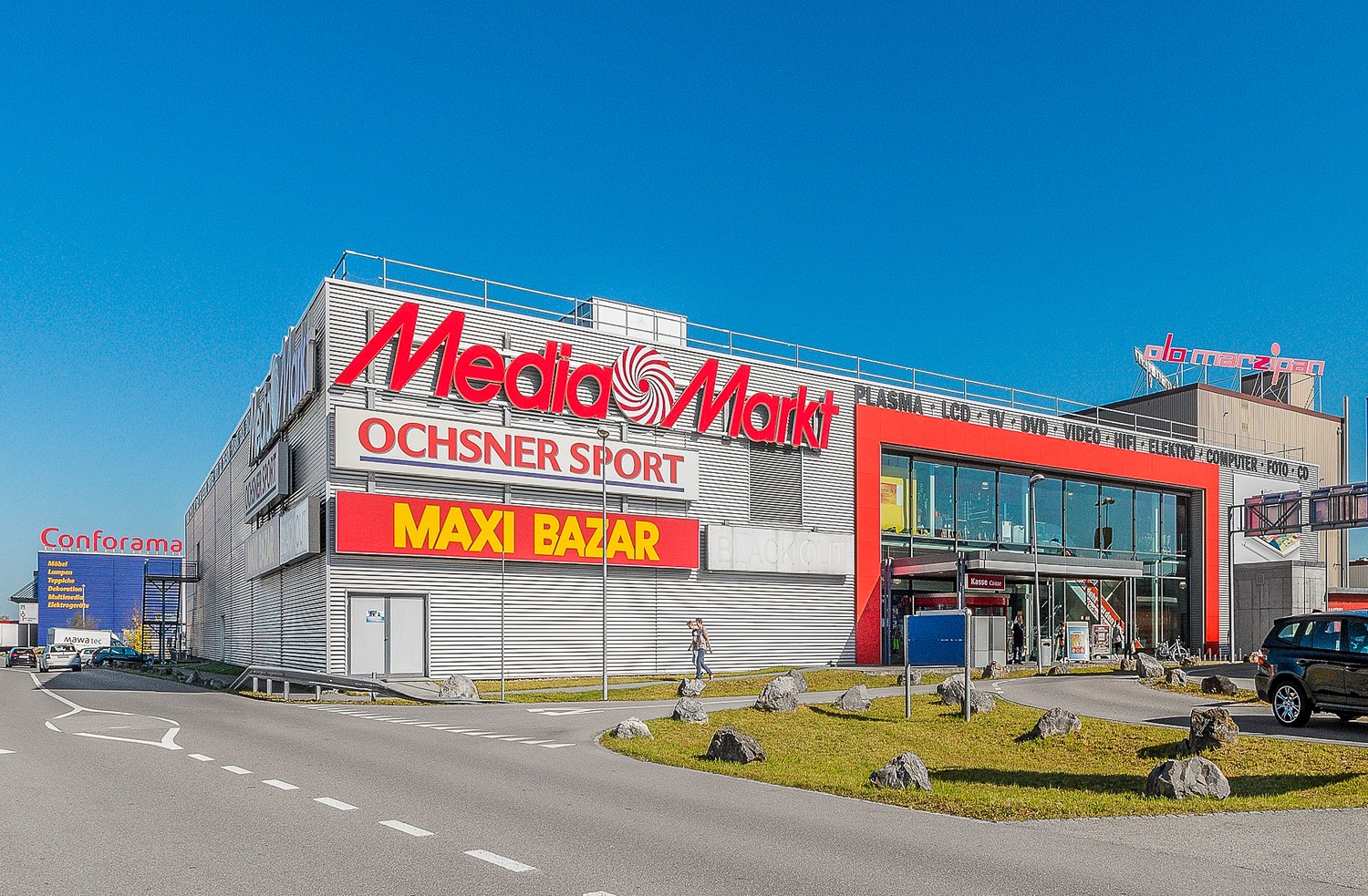 Retail complex with Media Markt, Ochsner Sport, and Maxi Bazar signage.