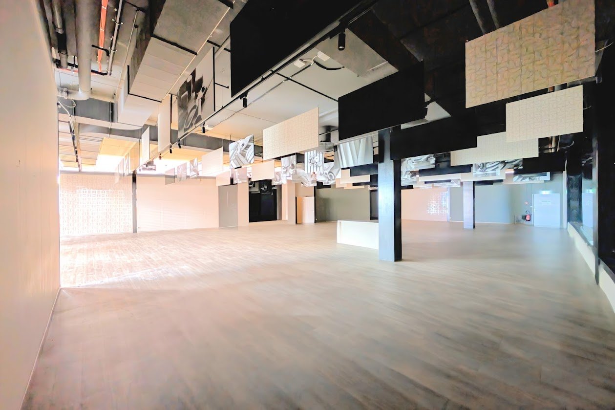 Empty room, hardwood floors, black pillars, white walls, hanging art panels, recessed ceiling lights.