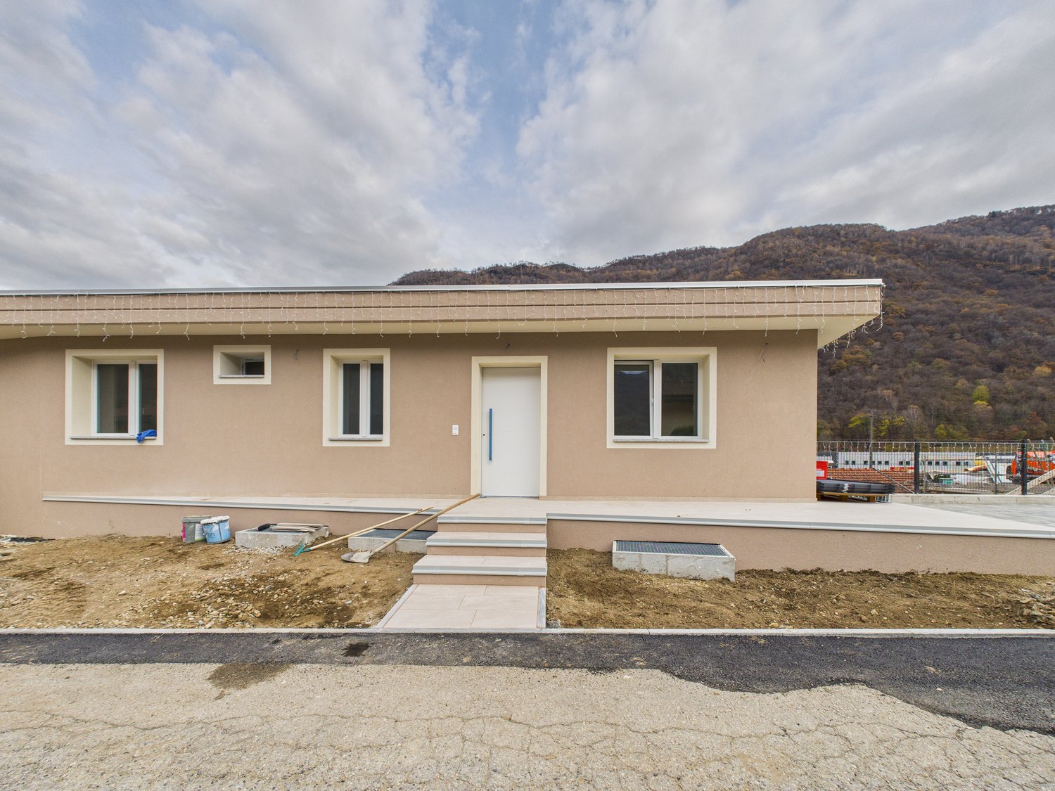Single story house, beige walls, white windows, sloped roof, tiled porch, mountain view in the background.