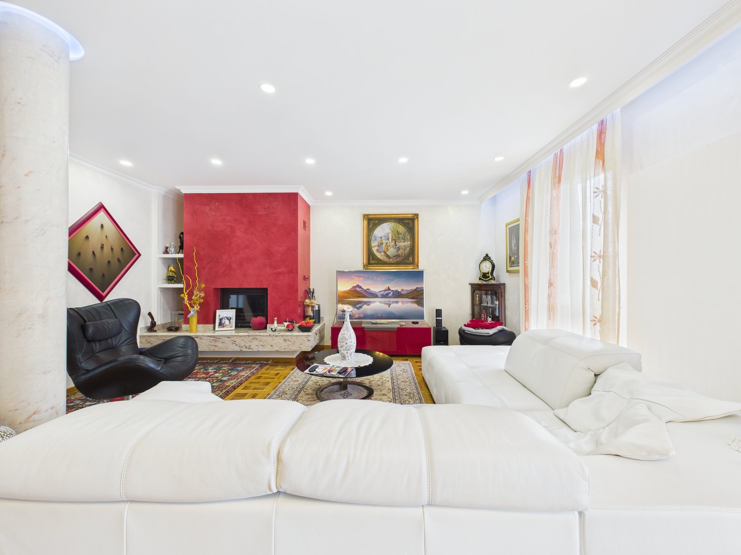 white leather sofa, black leather armchair, fireplace, flat screen TV, coffee table, rug, picture frames, shelves, clock