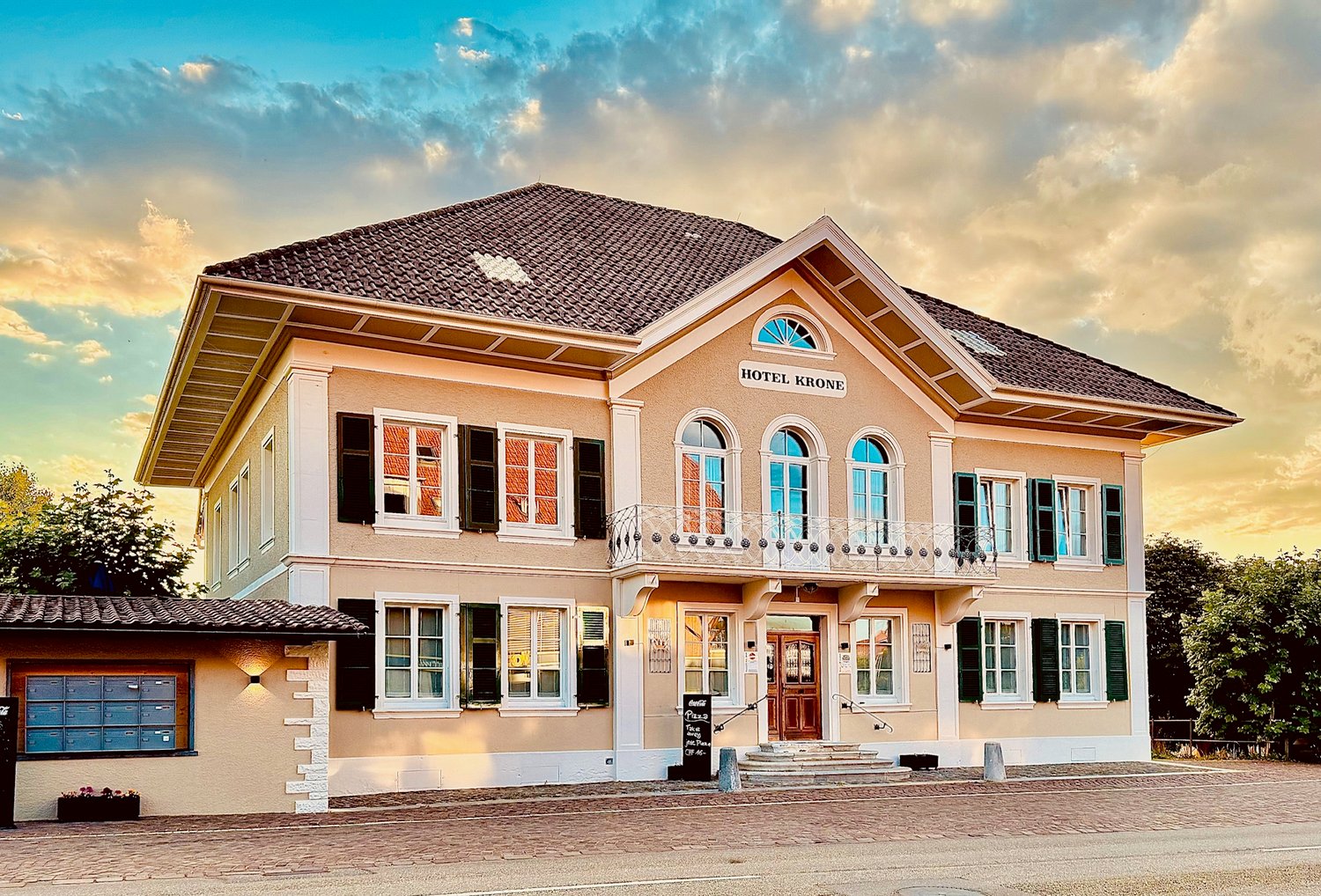 2 story hotel building, brown roof, beige facade, arched windows, balcony, entrance with stairs