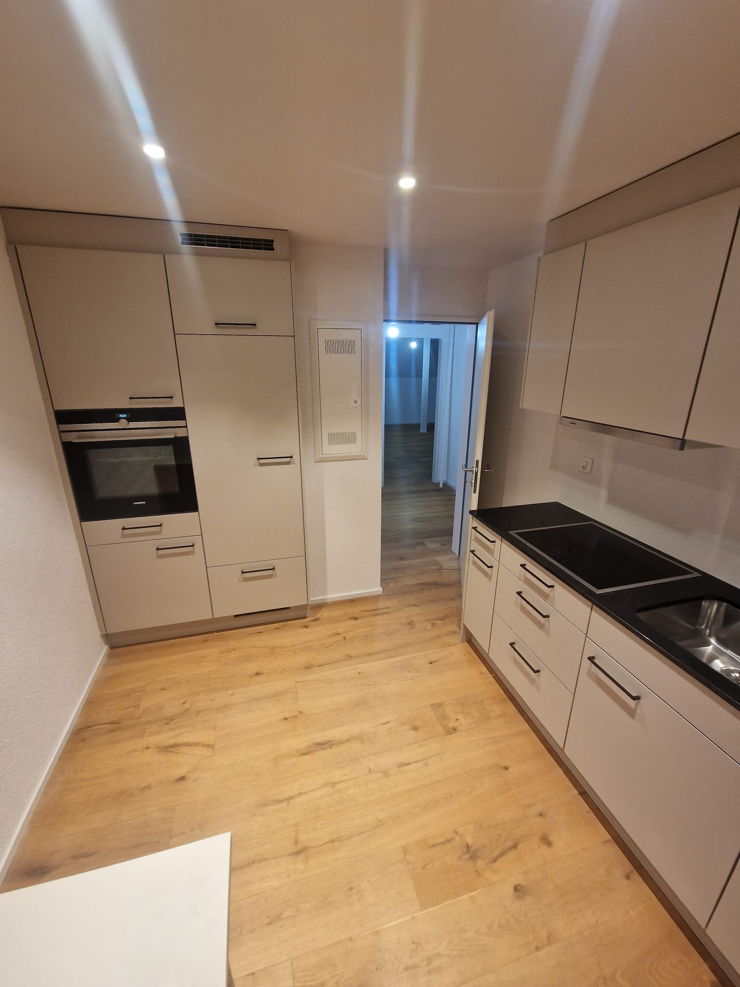 modern kitchen with wooden floor, white cabinets, black countertops, built-in oven, dishwasher, and sink