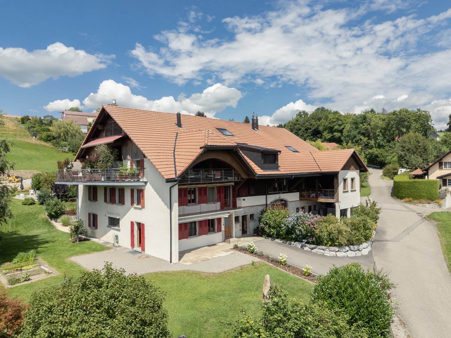 Two-story house, brown roof, white exterior, red shutters, multiple balconies, garden, driveway