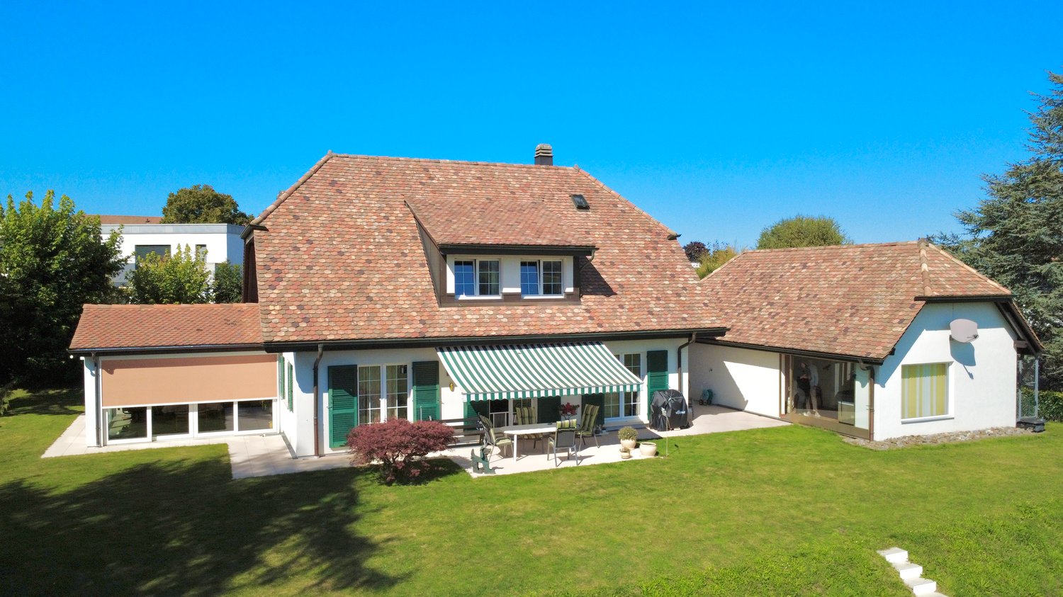two story house, brown tile roof, balcony, green lawn, exterior patio with table and chairs, awning, window view, outdoor plants