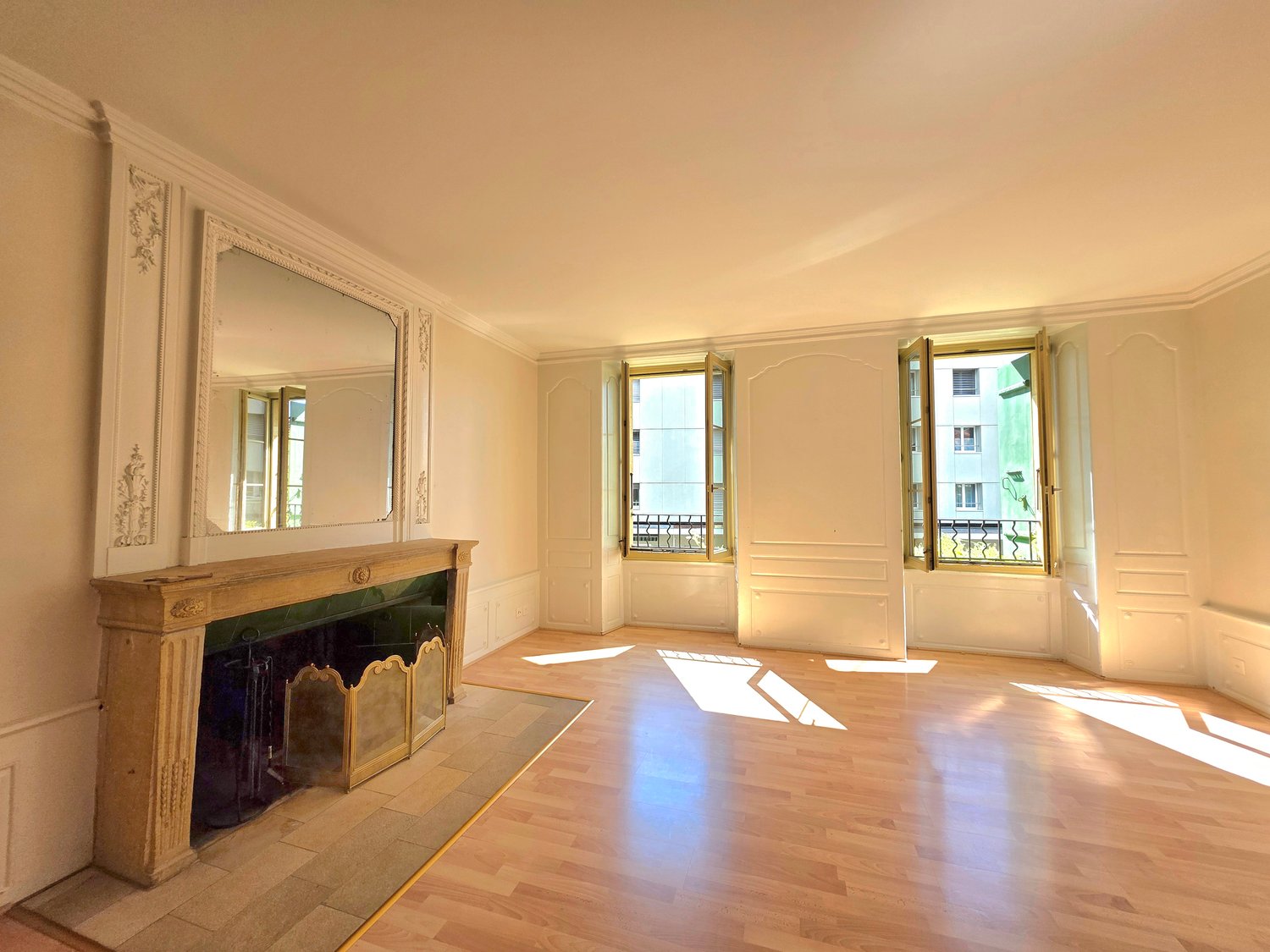 empty room with large fireplace, wooden floor, white walls, windows