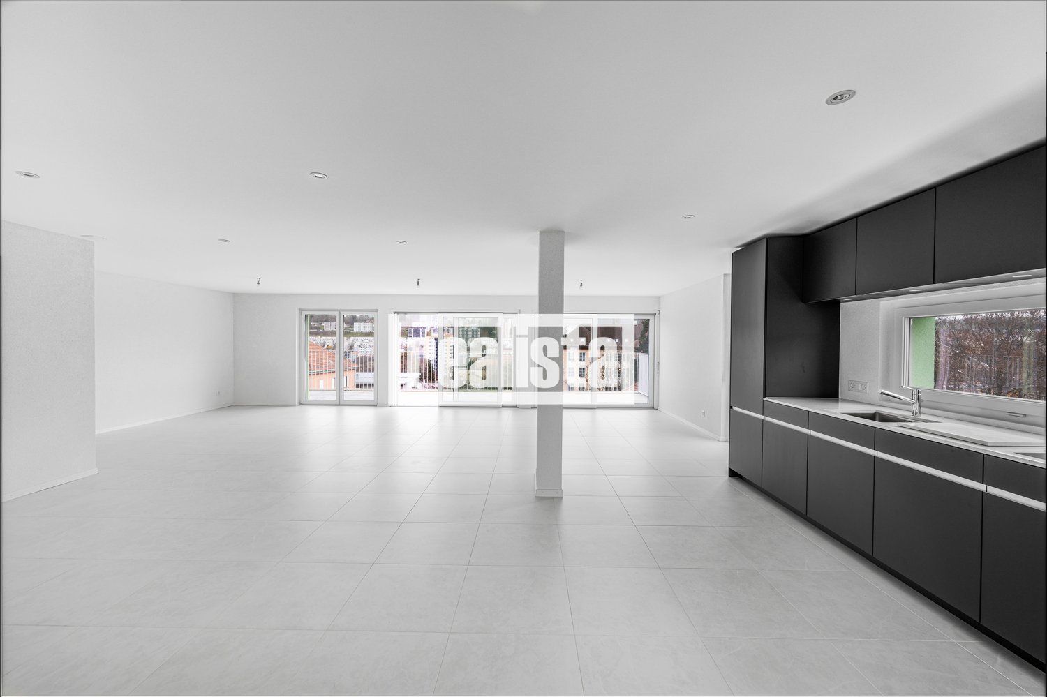 open space, large sliding glass doors, white tile floor, white walls, kitchen with sink, cabinets, and window