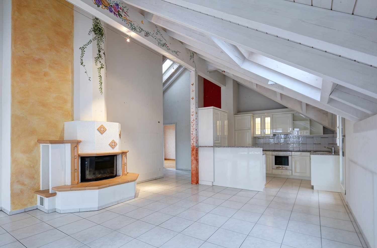 Empty room with a fireplace, kitchen with tiles, cabinets, and an oven, loft style ceiling with white trusses