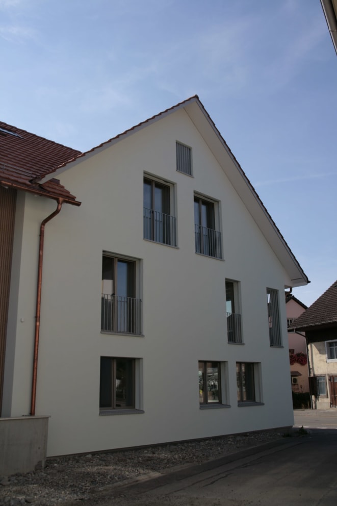 White apartment building, tiled roof, multiple glass windows with balconies, gutters