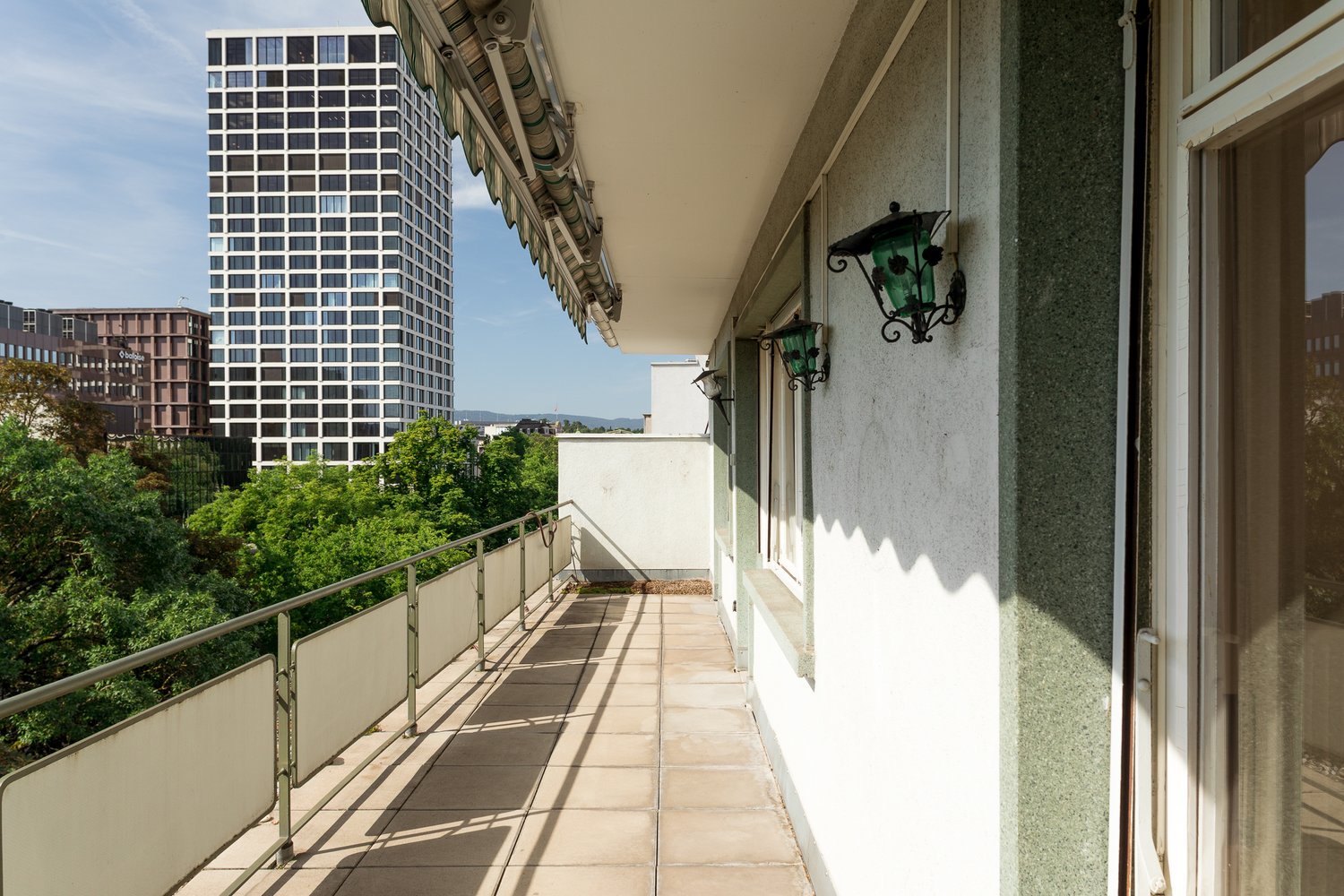 tiled floor, metal railing, large open area, green trees, modern buildings, blue sky