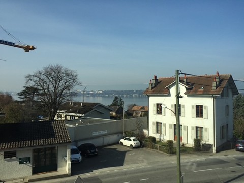White house, brown roof, cars parked in front, view of the lake in the distance