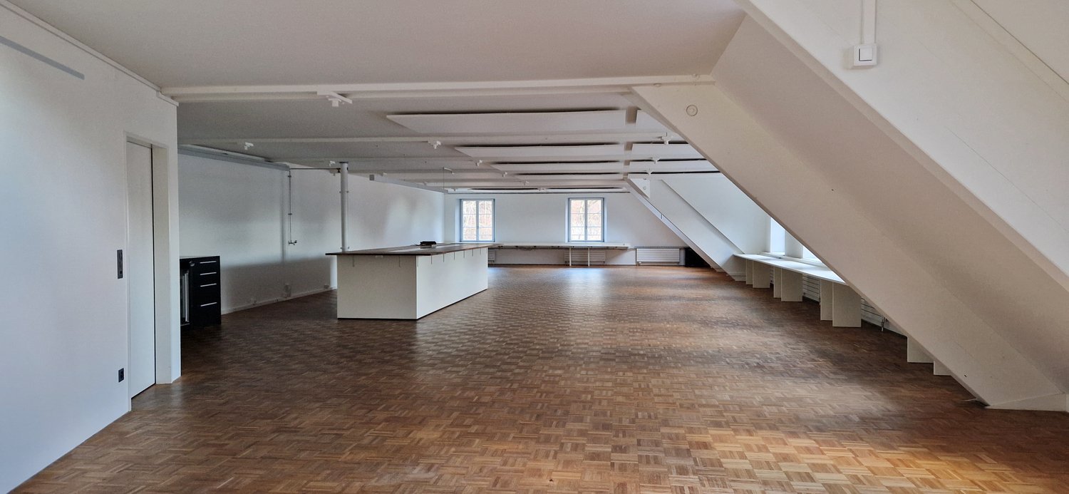 spacious room, wooden parquet floor, white walls, central white island counter, two small windows, built-in storage