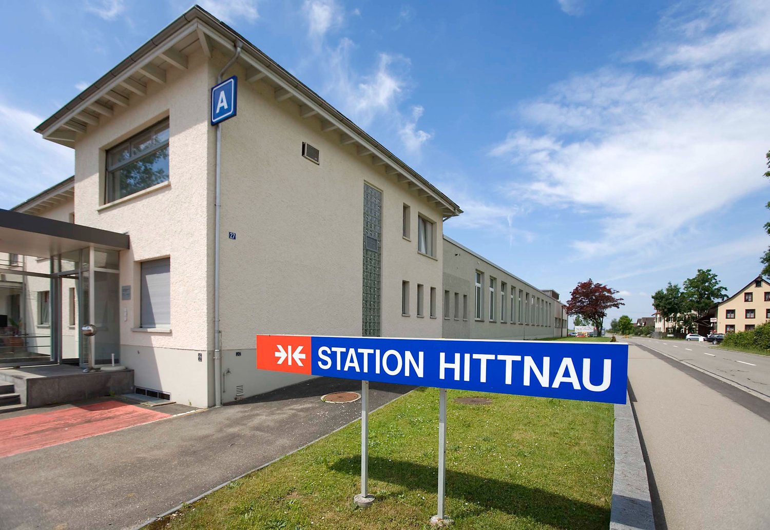 A building with a sign that reads 'Station Hittnau', a large window, and a red carpet leading to the entrance.