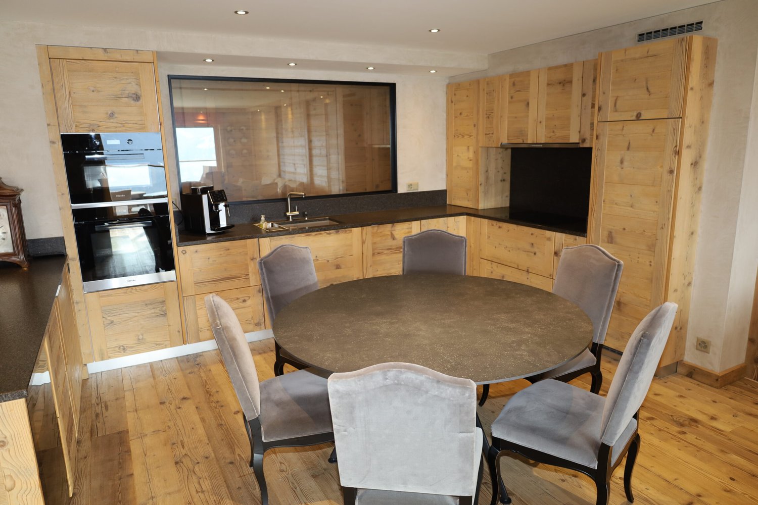 Modern kitchen with wooden cabinets, a round dining table, wooden floor, a sink with faucet, oven and refrigerator