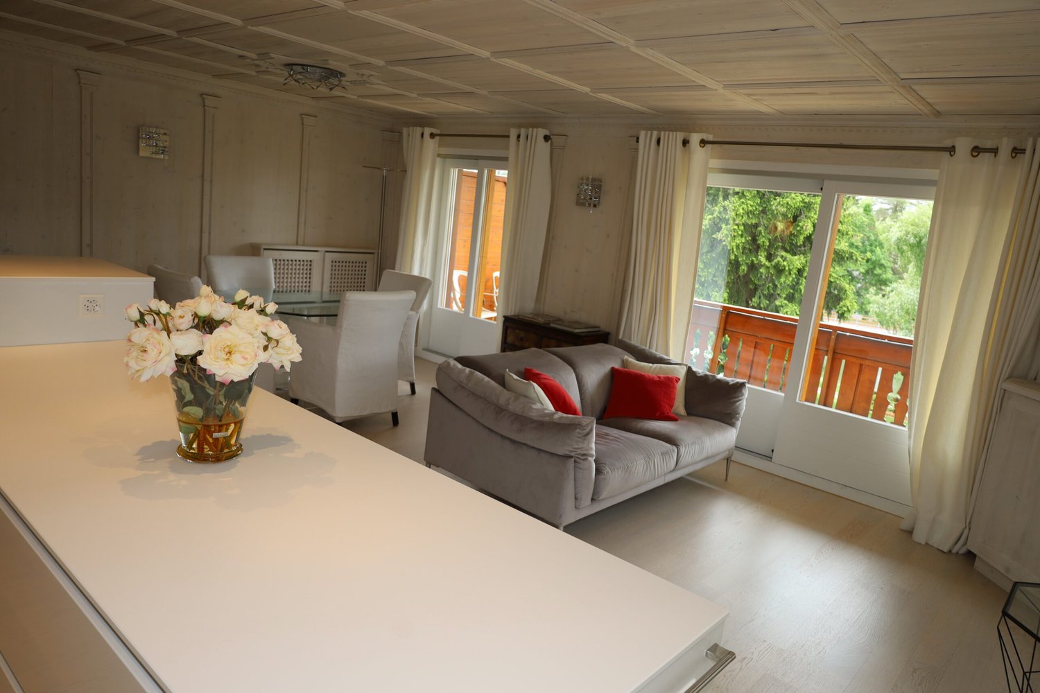 gray sofa, white chairs, glass table, flowers in a vase, sliding glass doors, balcony