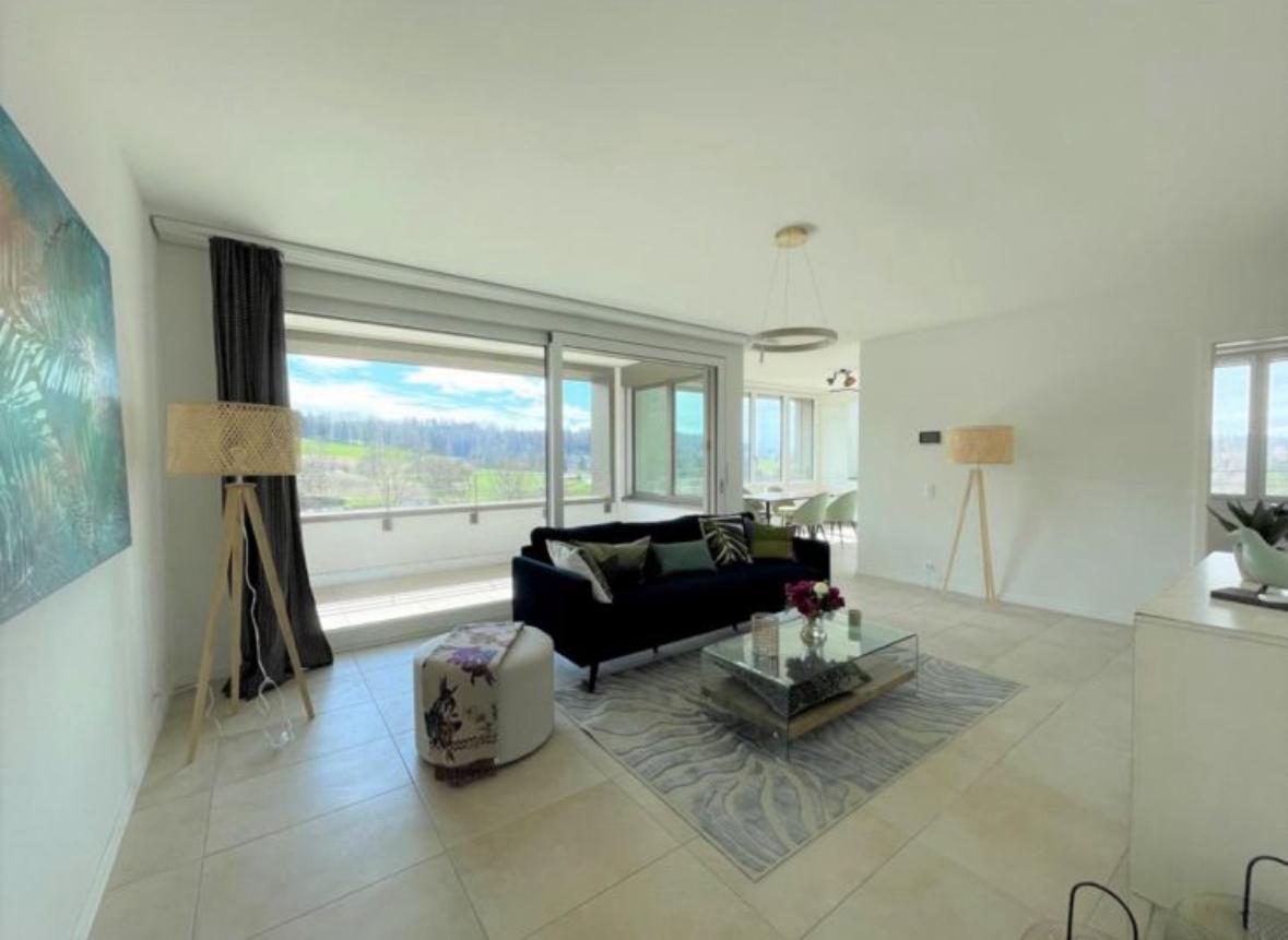 Spacious living room with large windows offering a scenic view, black sofa, glass coffee table, area rug, and decorative lamps