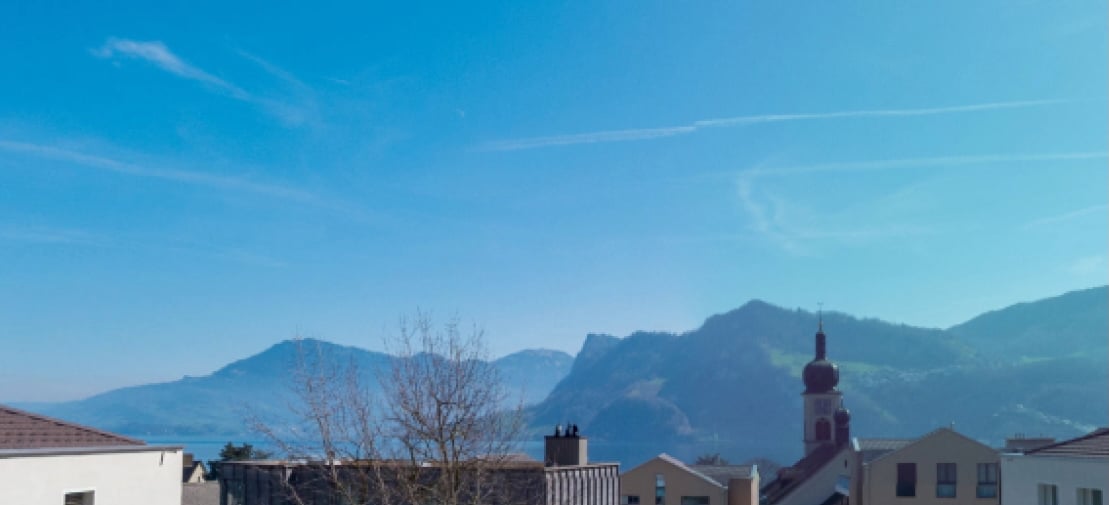 Aerial view of buildings, mountains, and water body, clear blue sky with some clouds