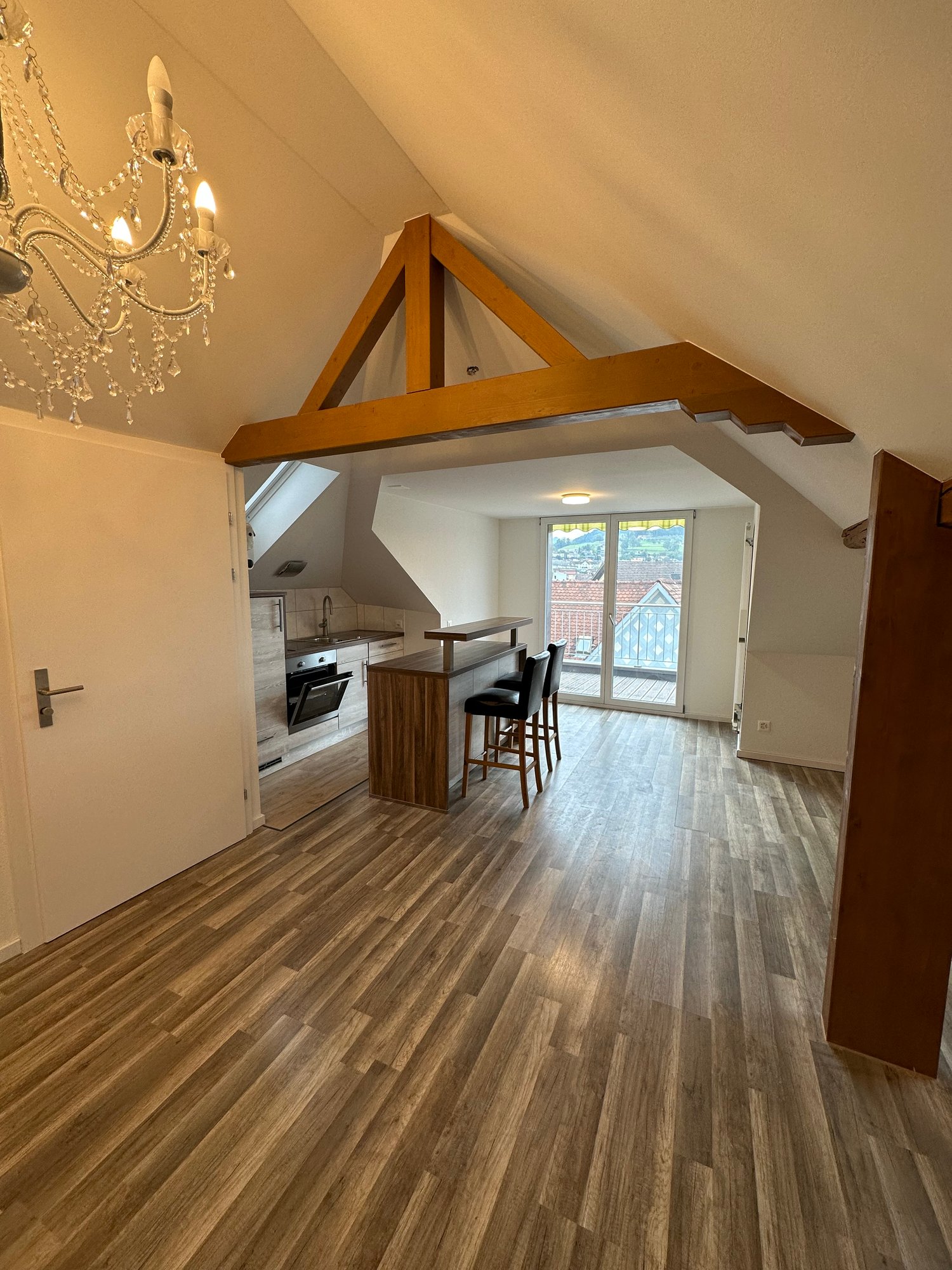 Open-concept living space with hardwood floors, wooden beams, kitchen with island, and access to a balcony or terrace.