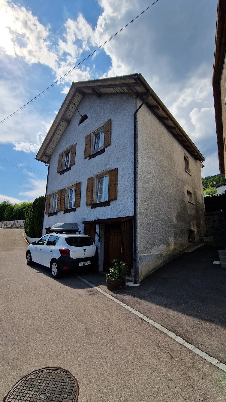 2-story house with gray exterior walls, brown wooden shutters, and a parked car in the driveway.