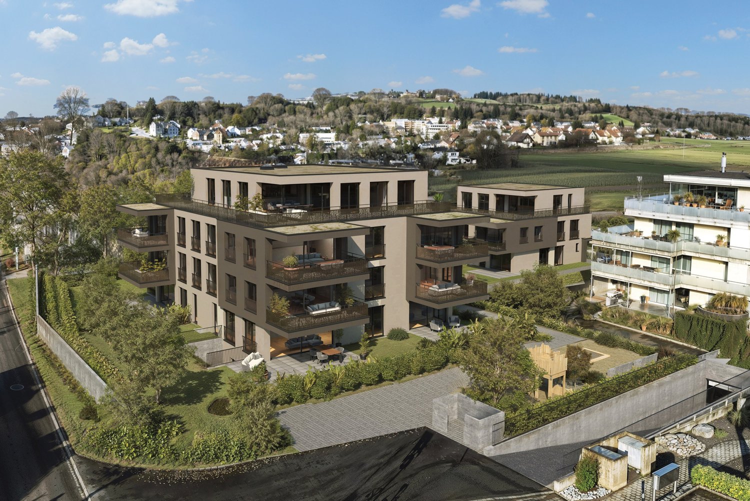 Multi-story apartment building with balconies, surrounded by landscaped gardens and parking spaces, overlooking a scenic town in the distance