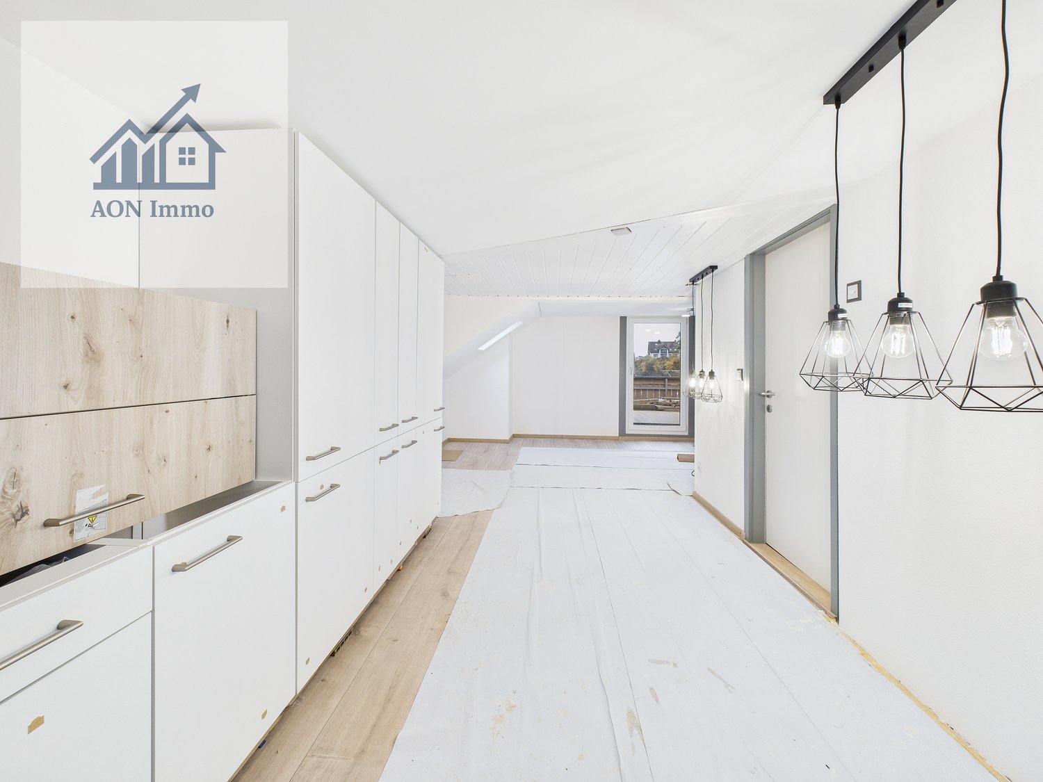 Empty room, modern decor, white walls, wooden floors, kitchen cabinets, suspended lamps, open doorway leading to another room.