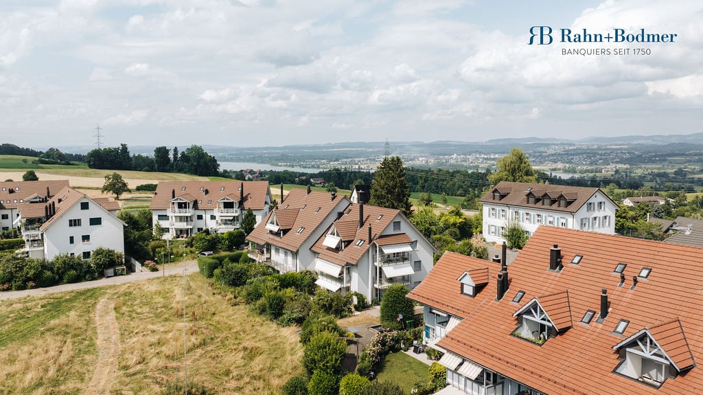 group of 9 apartments with brown roofs and white facades, hills, mountains, river in the distance
