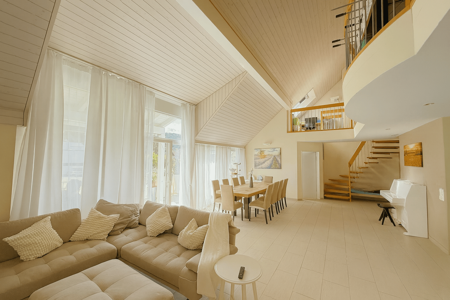 spacious living room with beige couch, white curtains, wooden staircase, dining table, piano, balcony