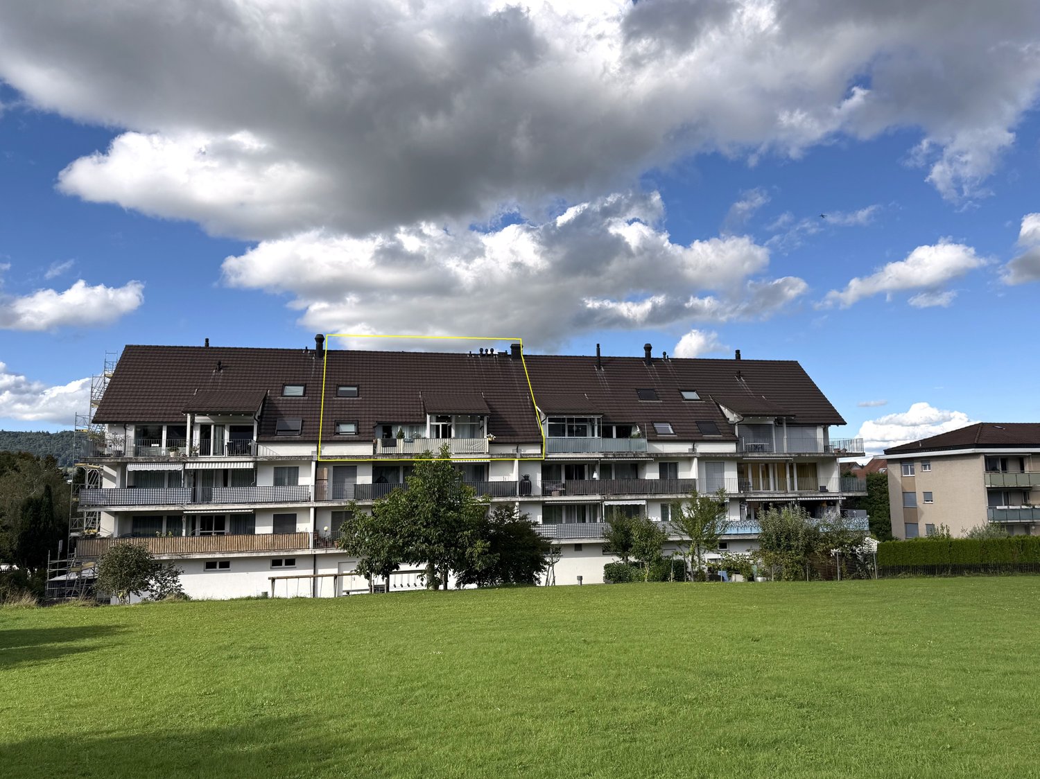 multi-story building with several balconies, brown roof, yellow highlight