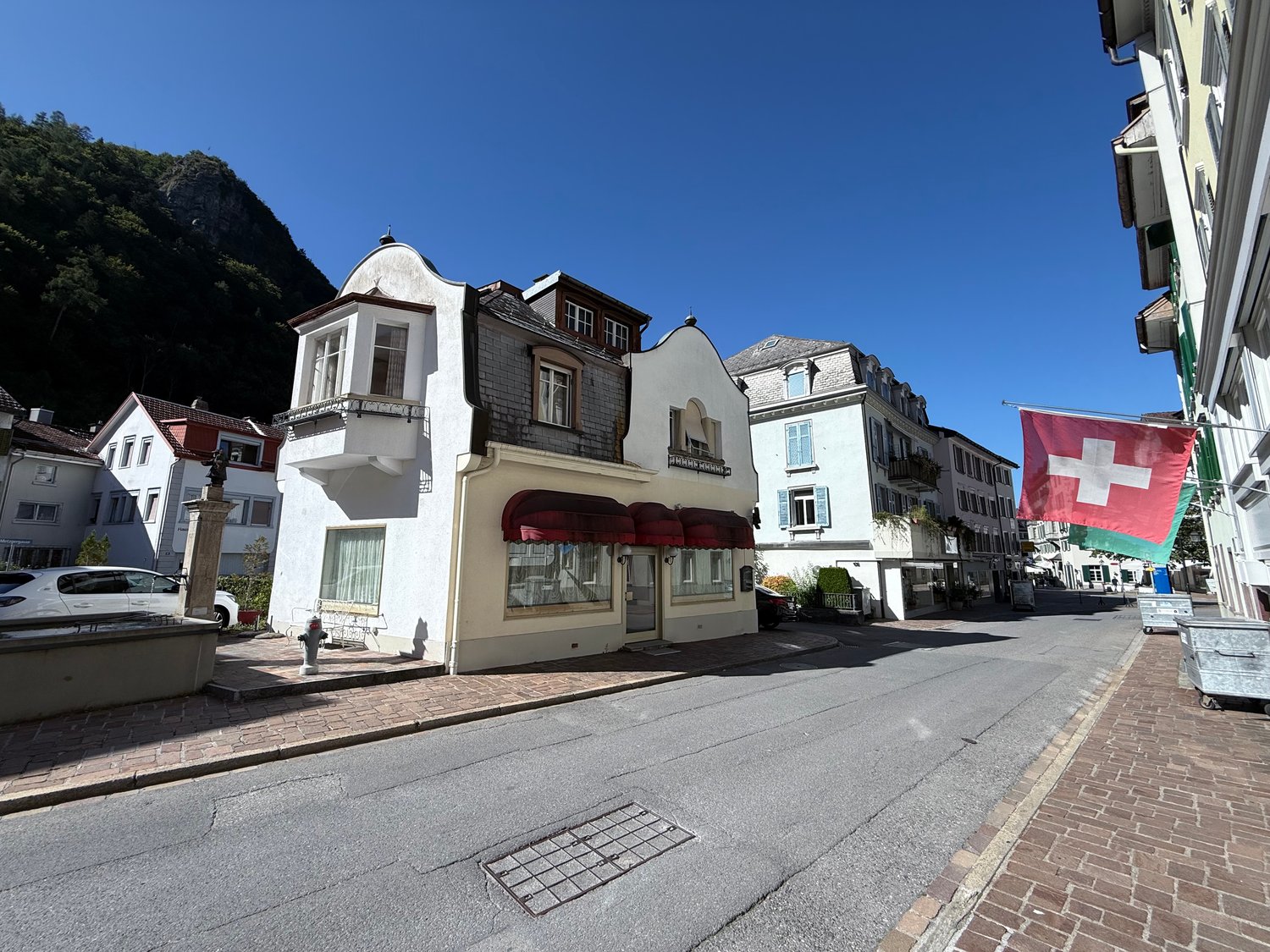Swiss house with white walls, red roofs, awnings, car parked in front