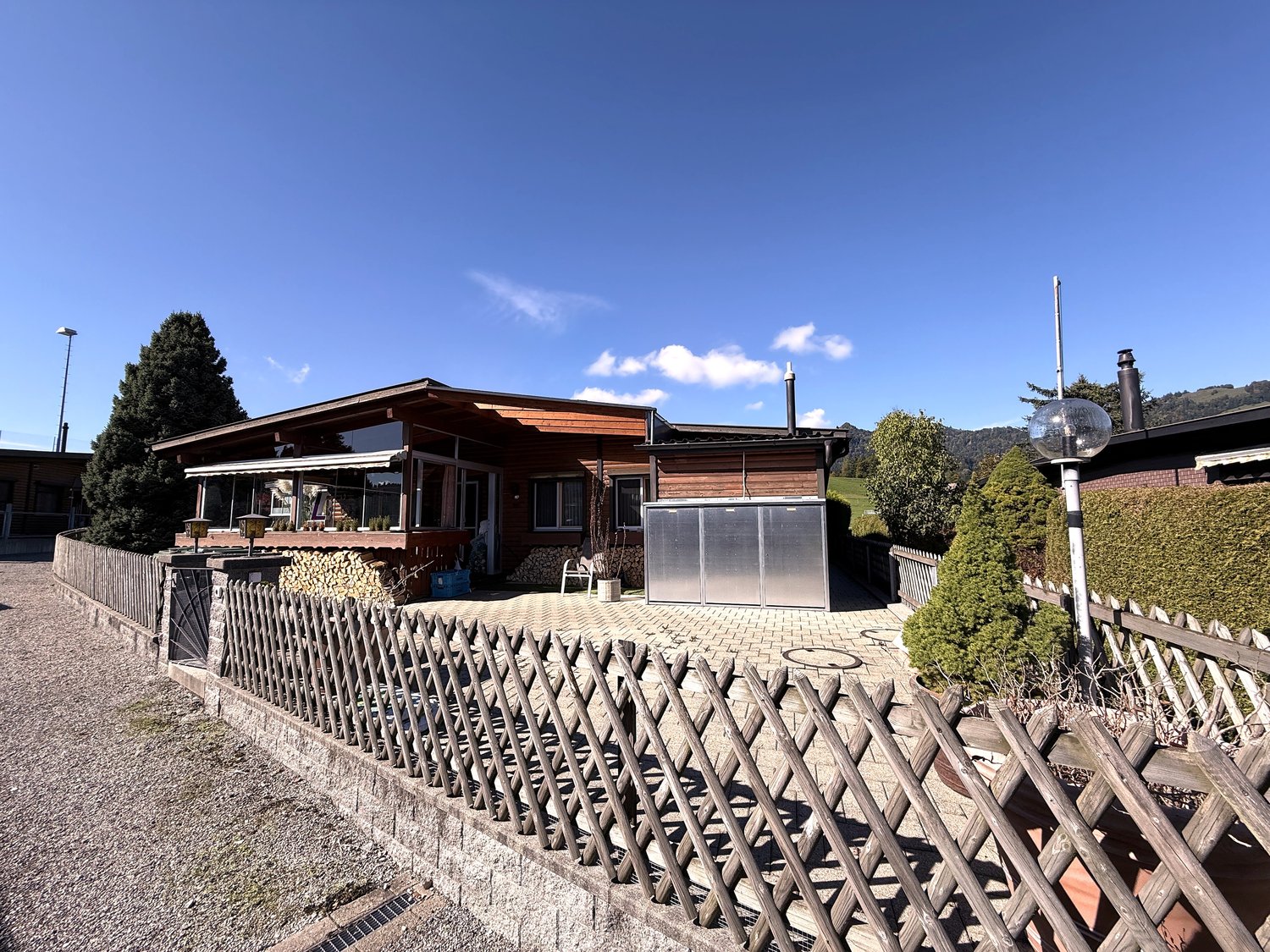 Wooden house, chimney, awning, garage, fence, shrub, tree