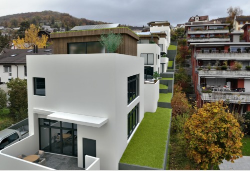 Modern terraced house, white exterior, large windows, solar panels on roof, raised ground floor, scenic mountain view