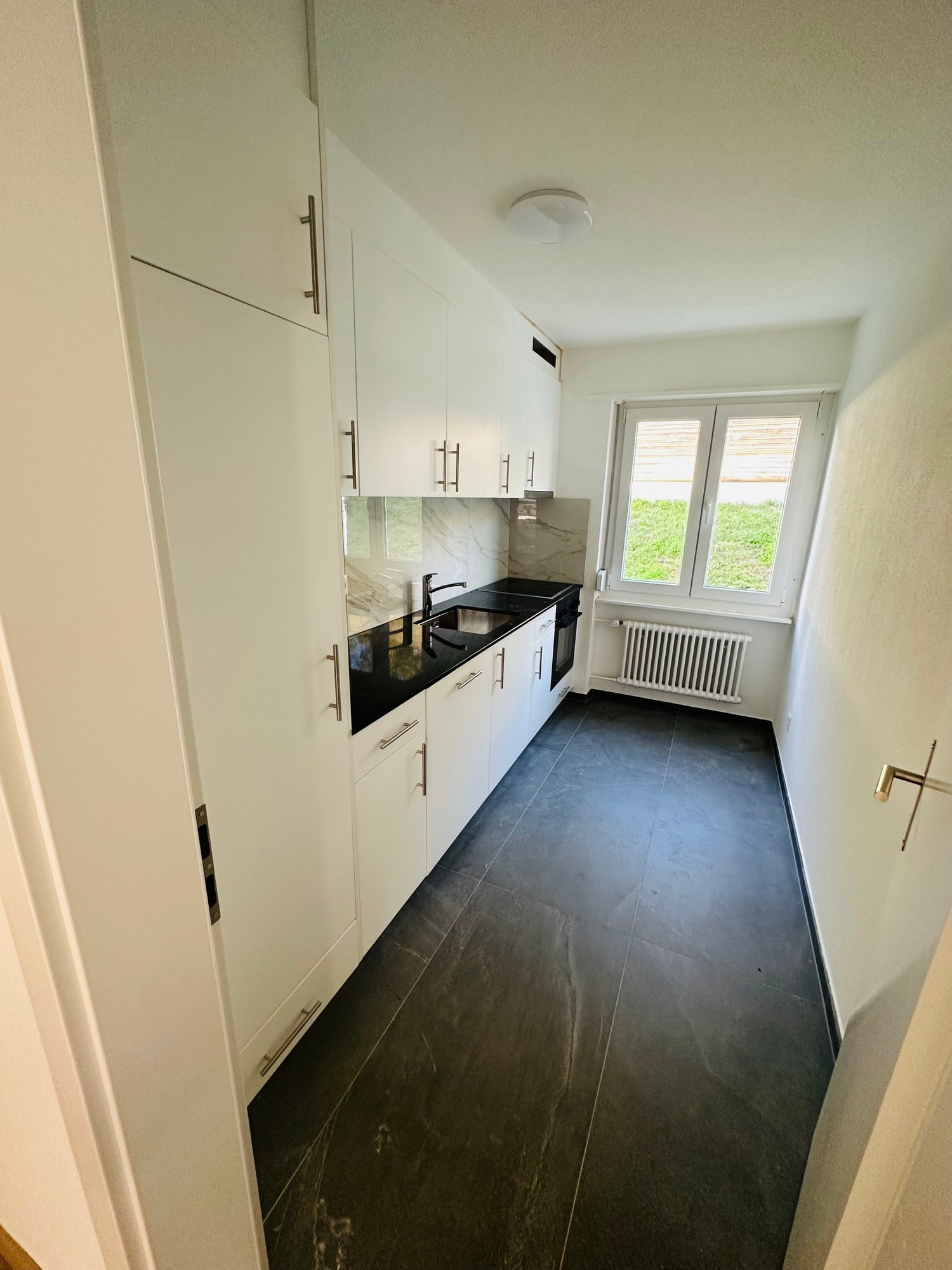 modern kitchen with black countertop, white cabinets, a sink with faucet, white radiator, and a black stove with an oven