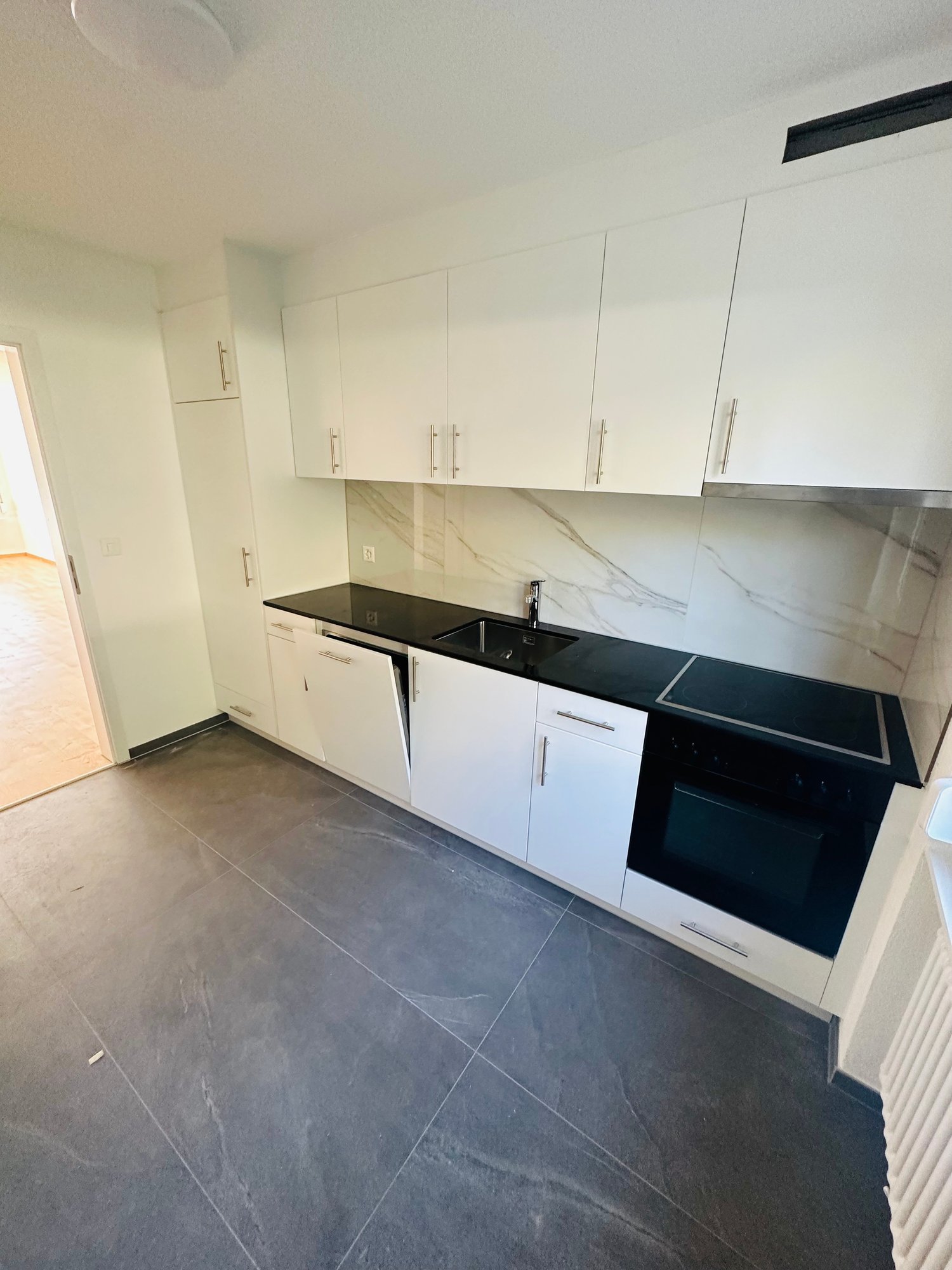 modern kitchen with granite floor, marble backsplash, white cabinets, black countertops, stainless steel sink, dishwasher, oven, and refrigerator