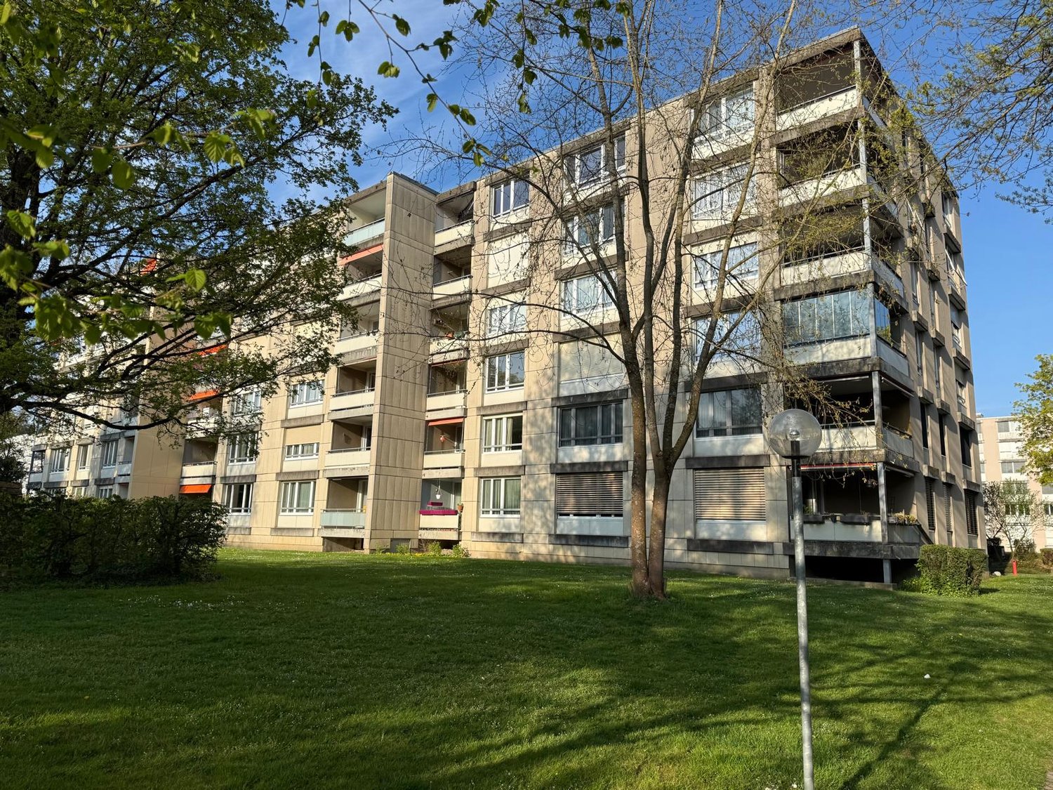 Multi-story apartment building with balconies, surrounded by trees and grass.