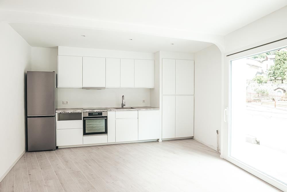 modern kitchen with white cabinets, stainless steel refrigerator, gas stove, sink, wooden flooring