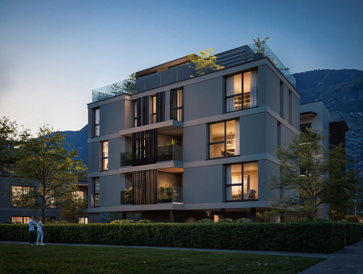 Modern multi-story building with glass balconies, illuminated windows, and a rooftop terrace with greenery.