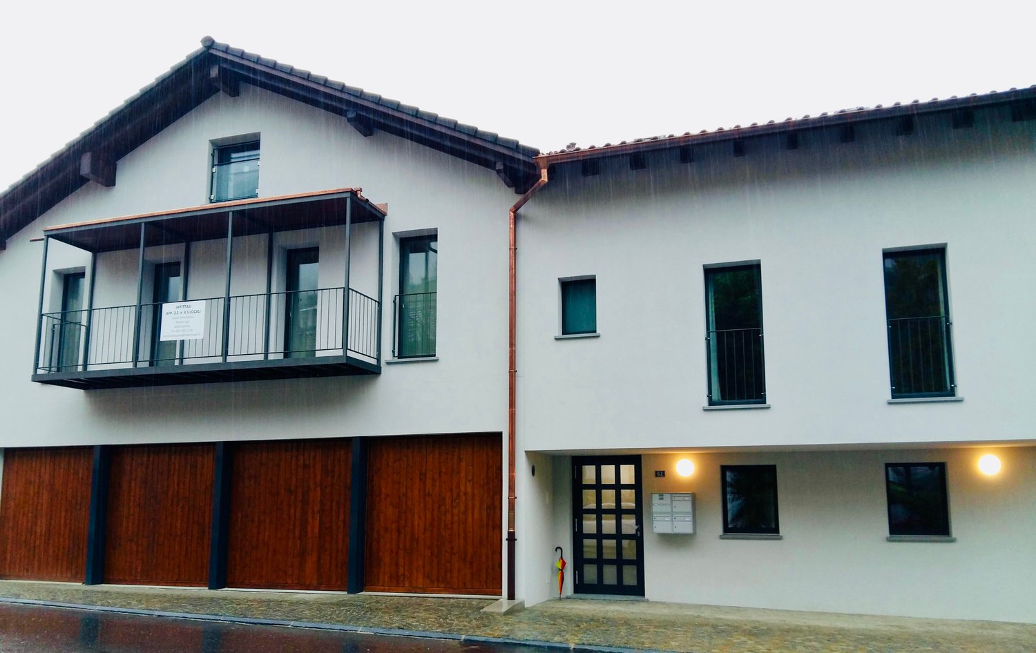 Two-story house, white exterior, brown wooden garage doors, balcony on the second floor, three windows on each floor
