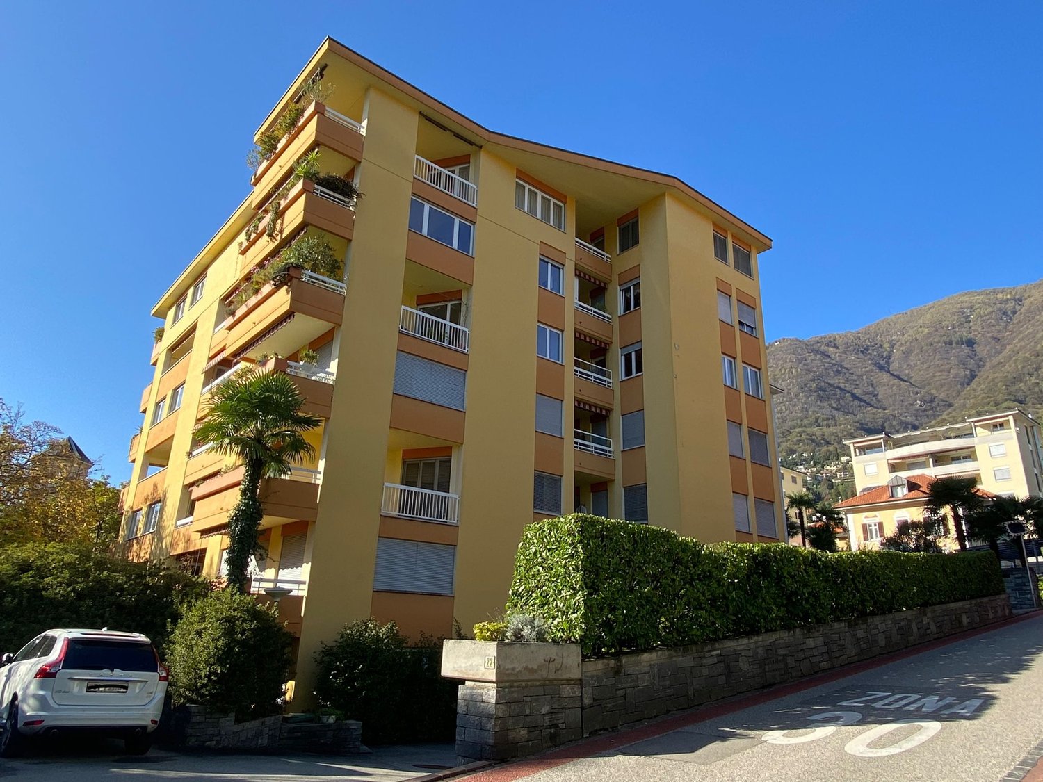 5 story apartment building, yellow exterior, balconies on each floor, garage on ground floor