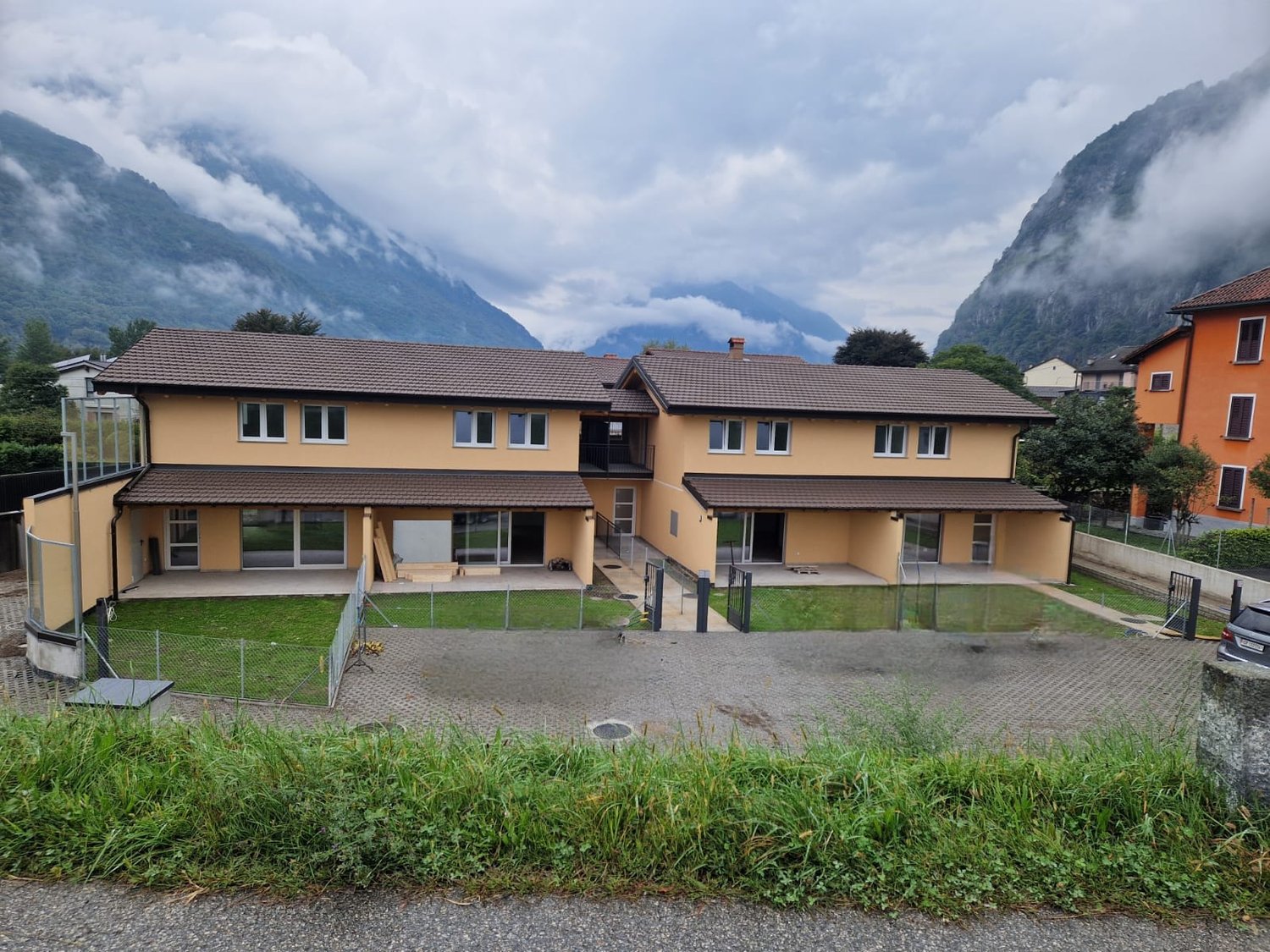 2 story house, yellow exterior, brown roof, large windows, fenced yard, mountains in the background
