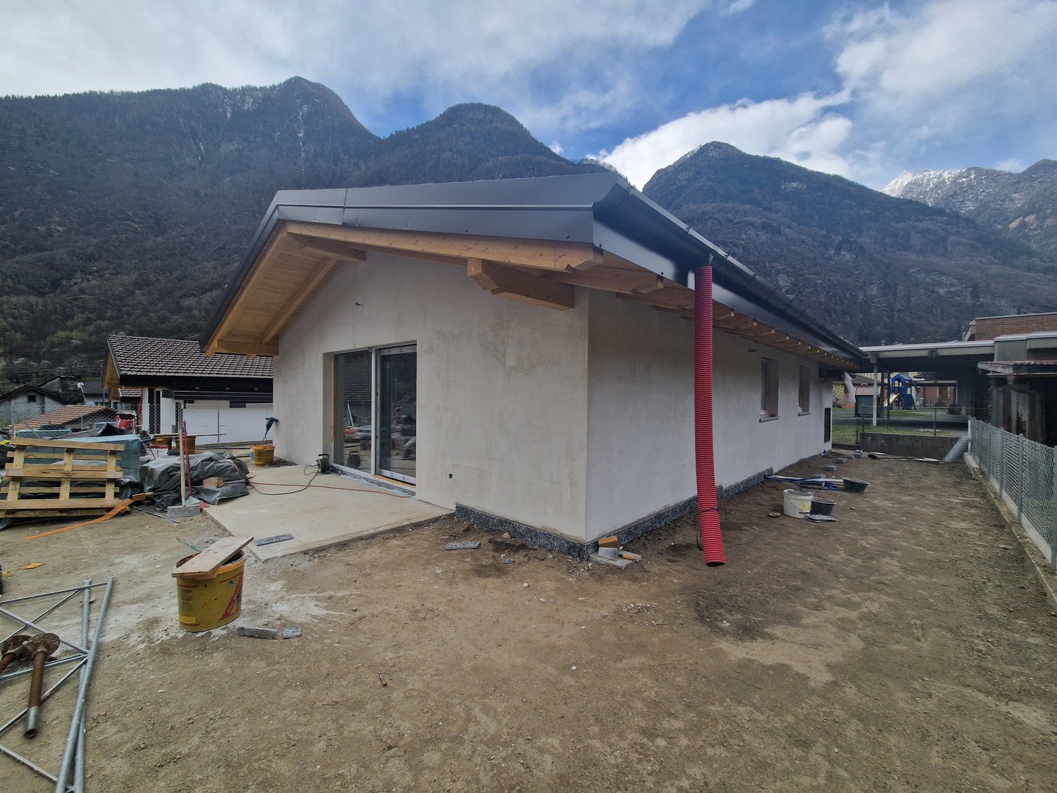 Newly constructed house, white exterior, gray roof, glass door, red chimney, construction materials around
