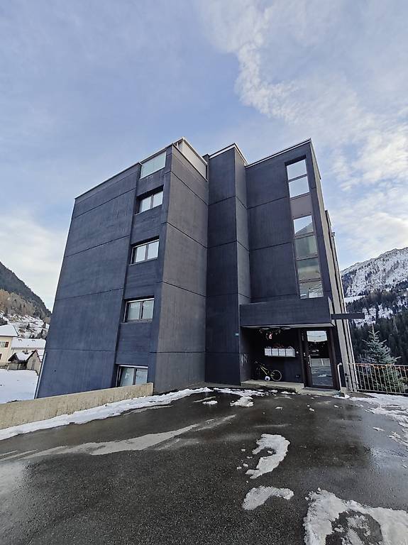 Modern multi-story building with multiple units, black exterior, several windows, entrance area, and a parking lot with a bicycle leaning against the building.