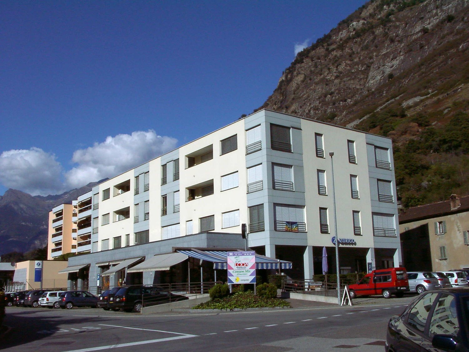 apartment building with balconies, several stories, cars parked in front