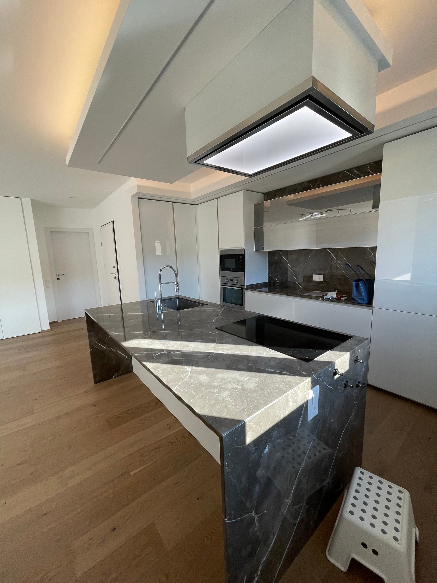 Open plan kitchen with marble countertops, two sinks, island, modern appliances, wooden floor, undermount lighting, cabinetry