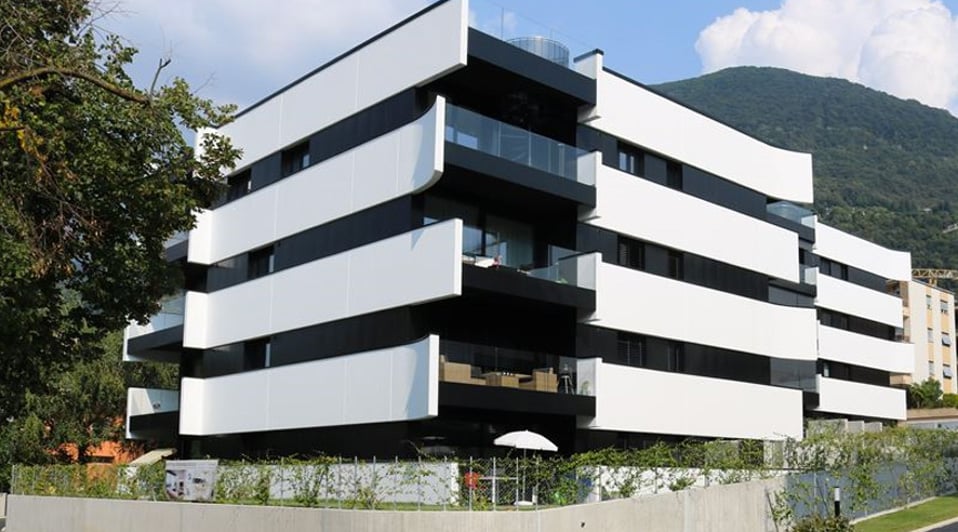 Modern apartment building with balconies, white exterior, 5 floors, trees, plants, fence, mountain view