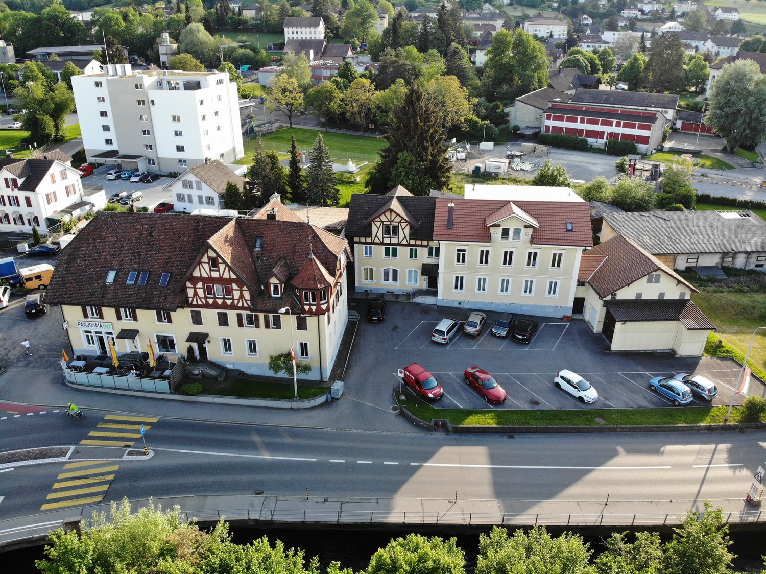 Multi-family building, two floors, multiple parking spaces, trees, and road