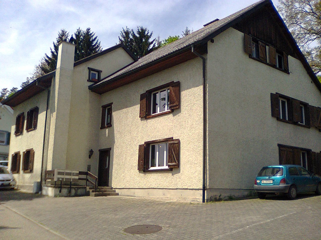 2 story house, beige walls, brown shutters, car parked in front, brick driveway