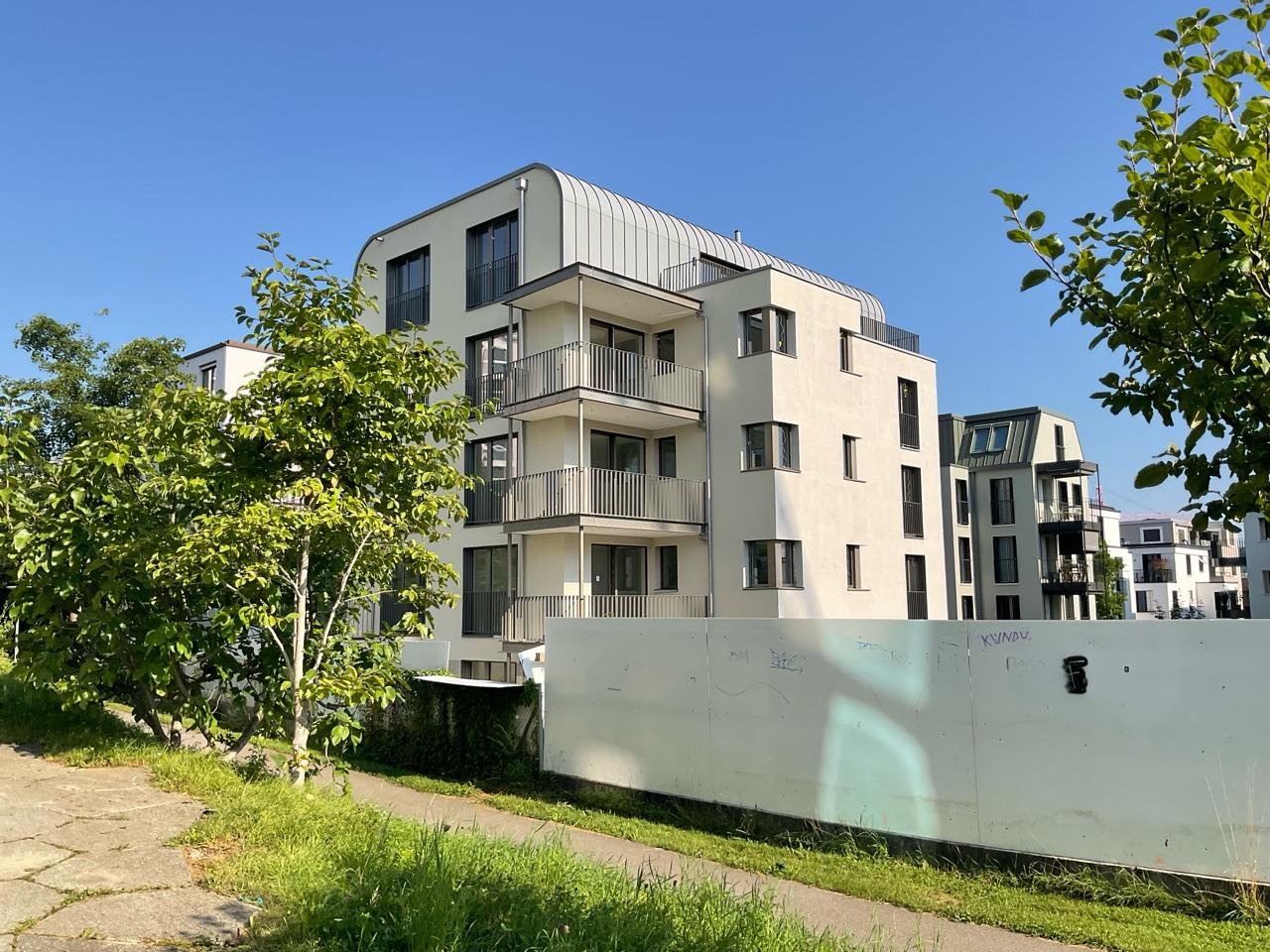 Multi-story building, white exterior, balconies, modern design, surrounded by greenery