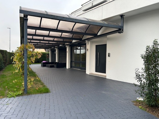 modern house with glass front, black awning, paved entrance, outdoor seating, white walls, garden