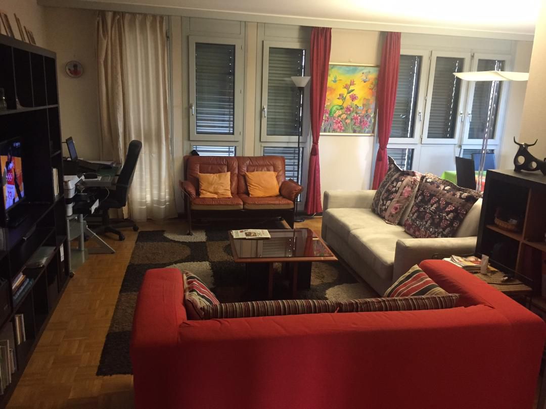 living room with two couches, two armchairs, coffee table, TV, computer desk, painting on wall, lamps, book shelves