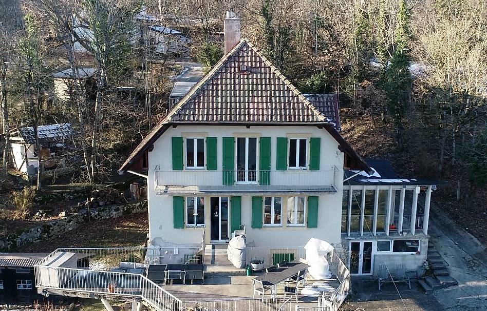 large house with a terrace and balcony, brown roof, white walls, green shutters